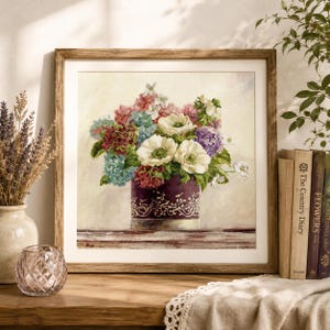 Puede incluir: Un bordado en punto de cruz con marco cuadrado que representa un ramo colorido de anémonas blancas, hortensias azules y flores rosas en un jarrón morado oscuro con un patrón de enredadera blanco sobre un fondo color crema.
