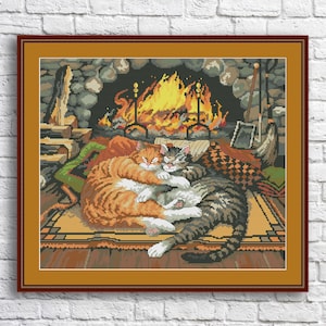 May include: Two cats cuddle together in front of a fireplace. The orange cat is on top of the gray and white cat. The fireplace has a roaring fire and a stone surround.