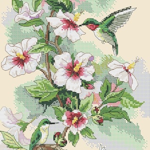 May include: A cross-stitch pattern featuring three hummingbirds with green and red plumage interacting with white hibiscus flowers with pink centres. One hummingbird is perched on a nest containing small eggs, while two others are in flight.