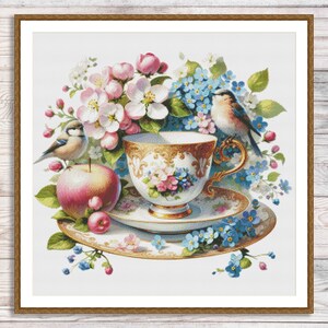 Puede incluir: Una delicada taza de té y platillo de porcelana con diseños florales, rodeados de flores de manzano rosas y blancas, nomeolvides azules y dos pájaros pequeños.