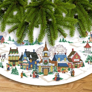 Könnte beinhalten: Ein weißer Christbaumrock mit einer gestickten Winterdorfszene. Die Szene zeigt Häuser, eine Kirche, ein Spielzeuggeschäft, einen Pavillon und Menschen, die im Schnee spazieren gehen. Der Text "Count Your Blessings" ist auf einem der Häuser gestickt.