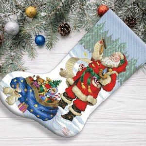 May include: A white Christmas stocking with a blue and white design. Santa Claus is depicted carrying a sack of toys and a list. The stocking is filled with toys, including a teddy bear, a doll, and a toy train.