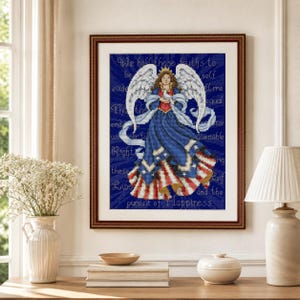 May include: A framed cross-stitch artwork featuring an angel with large white wings, wearing a blue dress with red and white stripes at the hem. The angel holds a white dove. The background is deep blue with text reading We hold these truths to be self evident that all men are created equal.