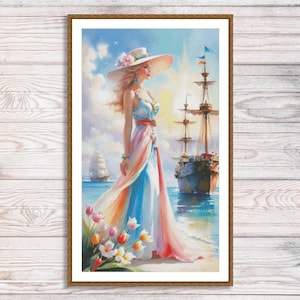 May include: A framed watercolor painting of a woman in a flowing dress and hat, standing on a beach. The dress is a mix of blue, pink, and orange. A sailboat and a large ship are in the background. Flowers are in the foreground.