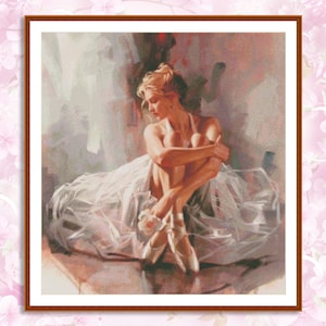 以下が含まれることがあります： 白いチュチュを着た若い女性が足を組んで座っており、ポアントシューズを履いています。背景は柔らかくぼやけており、ピンクと白です。