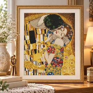 Puede incluir: Un cuadro de pintura de diamantes que representa a una pareja abrazada, inspirado en El Beso de Gustav Klimt. La obra presenta un patrón geométrico en dorado, amarillo y negro con detalles florales, en un marco dorado con borde blanco.