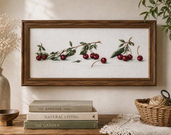 Może przedstawiać: Prostokątny haft krzyżykowy przedstawiający poziomy układ ciemnoczerwonych wiśni na zielonych łodygach z liśćmi, oprawiony w ciemnobrązową drewnianą ramę. Dzieło prezentuje szczegółowy wzór botaniczny na białym tle z tkaniny.