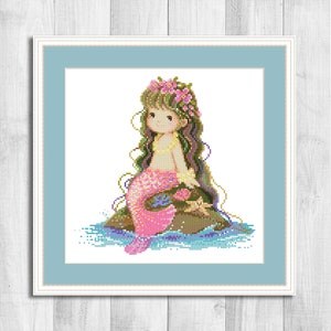 May include: A cross stitch pattern featuring a mermaid with long brown hair, a pink tail, and a flower crown. She is sitting on a rock with a starfish beside her.