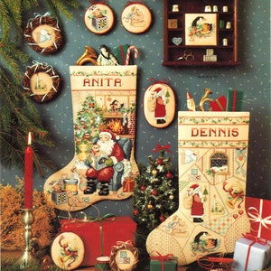 May include: A festive Christmas scene featuring two embroidered stockings, one labeled "ANITA" and the other "DENNIS", filled with gifts and decorations. Ornaments, a small Christmas tree, and wrapped presents complete the holiday display.