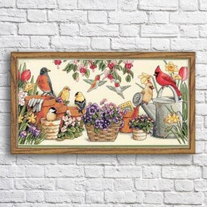 Könnte beinhalten: Ein gerahmtes Kreuzstich-Kunstwerk, das eine Gartenszene mit verschiedenen Vögeln, Blumen und einer Gießkanne zeigt. Zu den Vögeln gehören ein Rotkehlchen, Kolibris und gelbe Finkenvögel. Die Blumen sind in den Farben Rosa, Lila und Gelb gehalten. Die Gießkanne ist silberfarben mit einem roten Griff.