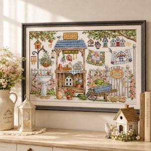 May include: A framed cross-stitch embroidery depicting a garden scene with a central herb stand, birdhouses, a birdbath, a wheelbarrow, and a gate. The text Nurture Nature is visible on a sign above the stand, and Welcome to My Garden is on the gate.