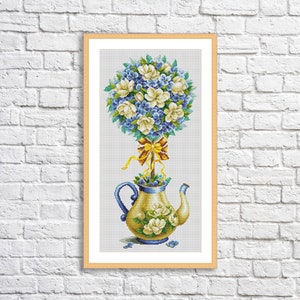 Peut inclure: Un motif de point de croix représentant un arrangement floral blanc et bleu dans une théière jaune et bleue. Les fleurs sont disposées en forme ronde, ressemblant à un topiaire.