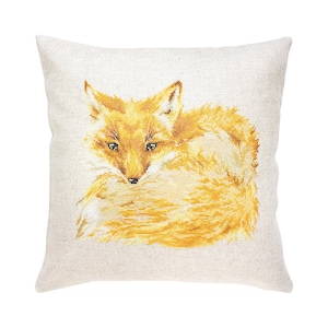May include: A decorative cushion featuring a cross-stitch design of a curled up orange fox. The fox is facing the viewer with its head tilted down. The cushion is made of a light beige fabric.