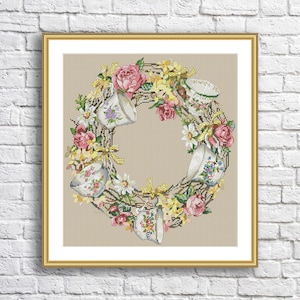 Puede incluir: Un patrón de punto de cruz que presenta una corona de tazas de té y flores. La corona está hecha de tazas de té blancas con diseños florales, rosas rosadas, narcisos amarillos y margaritas blancas. El fondo es una tela de lino beige.