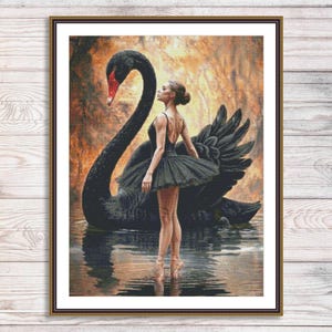 May include: A framed wall art print depicting a ballet dancer in a black tutu standing on water in front of a large black swan. The background features a warm, golden-toned forest setting. The dancer is positioned in profile, facing the swan.
