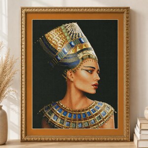 Puede incluir: Una impresión artística enmarcada que muestra el perfil de una persona con un tocado alto y ornamentado de varios colores y un collar ancho y decorativo. Las joyas presentan patrones geométricos en azul, dorado y verde sobre un fondo negro.