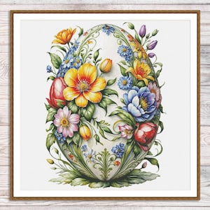 Puede incluir: Impresión enmarcada con un diseño floral de huevo de Pascua. El huevo está adornado con una variedad de flores coloridas, incluyendo flores amarillas, naranjas, rosas y azules, sobre un fondo blanco. La obra de arte está enmarcada en un marco de madera marrón.