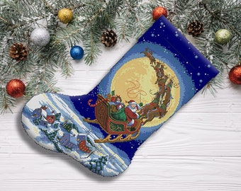 Könnte beinhalten: Ein blauer und weißer Weihnachtsstrumpf mit einem Weihnachtsmann und Rentieren, die in einem Schlitten durch die Luft fliegen. Der Strumpf ist mit einem Mond und Sternen verziert.