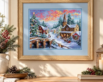 May include: A framed cross-stitch artwork depicting a snowy winter village scene at dusk. The image features a stone bridge, a large decorated Christmas tree, and buildings with snow-covered roofs under a vibrant pink and orange sunset sky.
