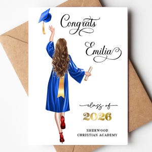 May include: A graduation card with a drawing of a graduate in a blue gown throwing their cap in the air. The card reads "Congrats Emilia" and "class of 2026" with the school name below. The card is on a brown envelope.