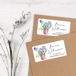 May include: Two white return address labels with a watercolor illustration of a potted plant with purple flowers and blue butterflies. The text on the label reads "Briana Williamson, P.O. Box 2152, Running Springs, CA 92382."