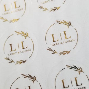 May include: A sheet of round, clear stickers with gold foil lettering and a leafy design. The stickers say "L|L Larry & Lauren".