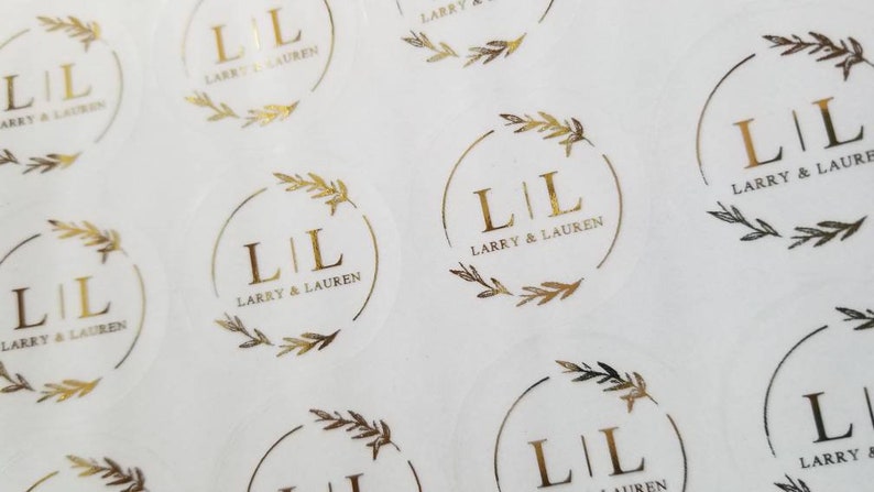 May include: A sheet of round, clear stickers with gold foil lettering and a leafy design. The stickers say "L|L Larry & Lauren".