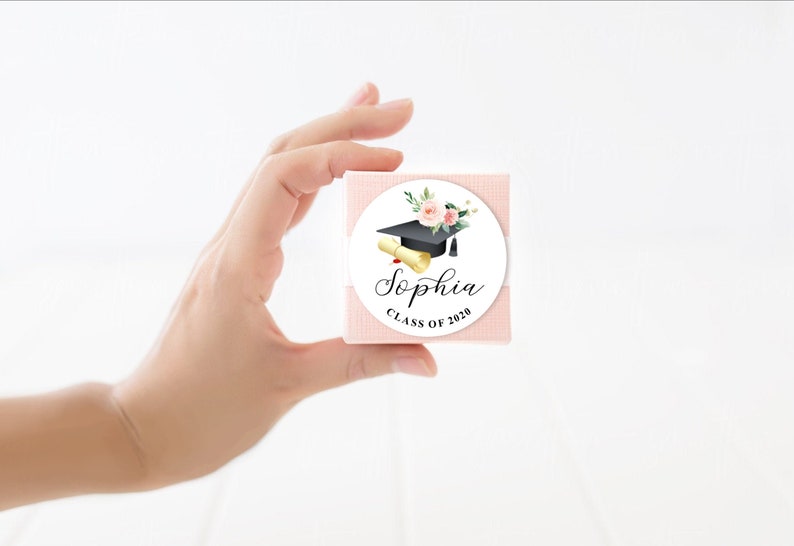 May include: A white round sticker with a black graduation cap, a gold scroll, and pink flowers. The text "Sophia Class of 2020" is printed on the sticker.