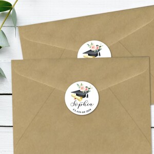 May include: Two brown envelopes with round white graduation stickers. The stickers feature a black graduation cap, a diploma, pink flowers, and green leaves. The text on the sticker reads "Sophia Class of 2020".