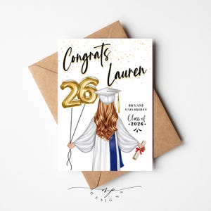 May include: A graduation card with the text "Congrats Lauren" and a gold foil balloon that reads "26". The illustration features a graduate in a cap and gown holding a diploma. The card is on a brown envelope.
