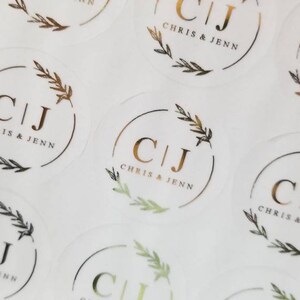 May include: A sheet of clear round stickers with gold foil lettering. The stickers feature the initials "C|J" with the text "Chris & Jenn" below. The initials are surrounded by a gold foil wreath.