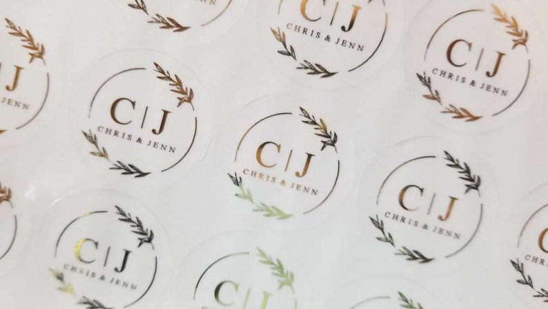 May include: A sheet of clear round stickers with gold foil lettering. The stickers feature the initials "C|J" with the text "Chris & Jenn" below. The initials are surrounded by a gold foil wreath.