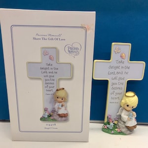 Könnte beinhalten: Eine Precious Moments Kreuzfigur und die dazugehörige weiße Schachtel. Das Kreuz hat einen hellblauen Hintergrund, einen gelben Rand und einen blonden Engel, der auf einem Felsen sitzt. Der Text lautet: Take delight in the Lord, and he will give you the desires of your heart. Psalm 37:4.