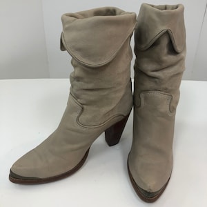 May include: A pair of light brown leather cowboy boots with a pointed toe and a stacked heel. The boots have a slouchy, folded-down top.