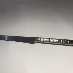 May include: A silver butter knife with a decorative, textured handle. The blade is serrated and the handle has a geometric pattern.