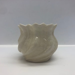 Puede incluir: Un jarrón de cerámica blanco con un diseño de remolino y textura. El jarrón tiene forma de flor.