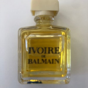 Peut inclure: Un flacon de parfum en verre transparent avec un bouchon en plastique blanc. Le flacon porte une étiquette sur laquelle est inscrit "Ivoire de Balmain".
