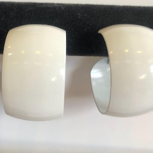 May include: A pair of off-white, chunky hoop earrings. The earrings have a rounded, rectangular shape with a curved opening. The interior of the earrings is a lighter shade of white.