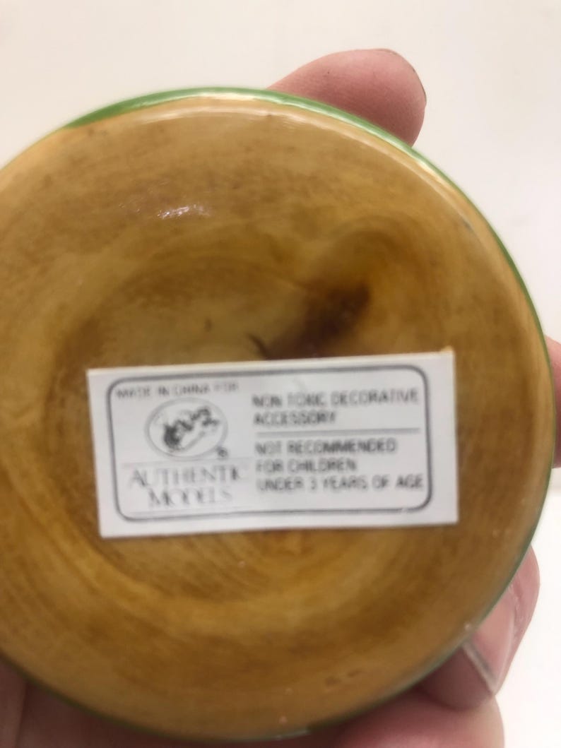 Op de afbeelding: Een houten decoratief accessoire met een lichtbruin interieur en een groene rand. De onderkant van het accessoire heeft een wit label met de tekst "NON TONIC DECORATIVE ACCESSORY" en "NOT RECOMMENDED FOR CHILDREN UNDER 3 YEARS OF AGE."