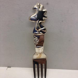 May include: Silver fork with a detailed design of a cartoon bird on the handle.