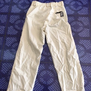 Op de afbeelding: Een licht beige, lichtgewicht broek met een elastische tailleband en een klein zwart label op de rechter achterzak. De broek heeft een ontspannen pasvorm en een licht verkorte lengte.