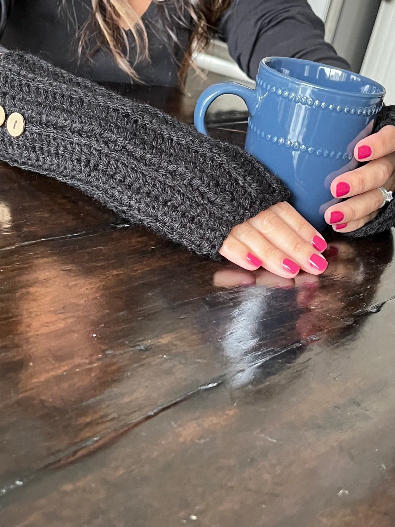May include: A close-up of a person's hand wearing a gray knitted fingerless glove, holding a blue ceramic mug with a beaded rim. The mug is filled with a warm beverage.