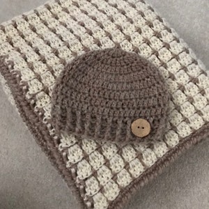 May include: A brown and white crocheted baby blanket with a matching brown crocheted hat. The hat has a brown button on the top.