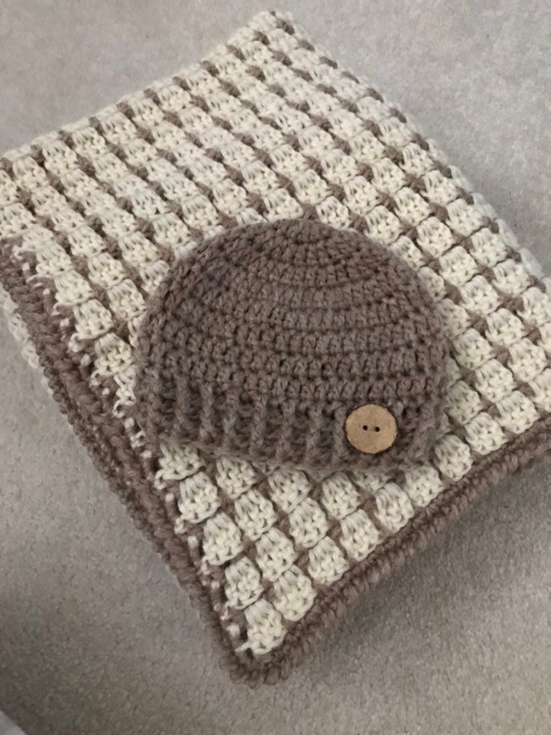 May include: A brown and white crocheted baby blanket with a matching brown crocheted hat. The hat has a brown button on the top.