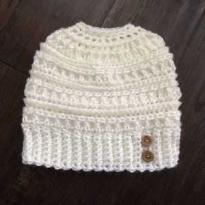 May include: White crocheted beanie with two brown buttons.
