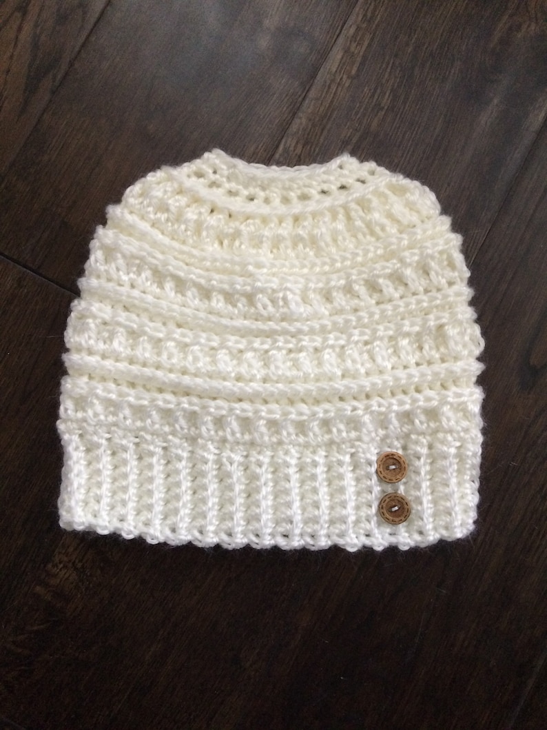 May include: White crocheted beanie with two brown buttons.
