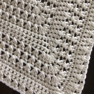 May include: White crocheted blanket with a delicate, intricate pattern. The blanket is made with a soft, lightweight yarn and has a smooth, even texture.