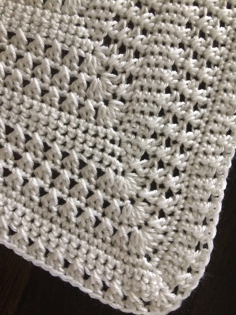 May include: White crocheted blanket with a delicate, intricate pattern. The blanket is made with a soft, lightweight yarn and has a smooth, even texture.