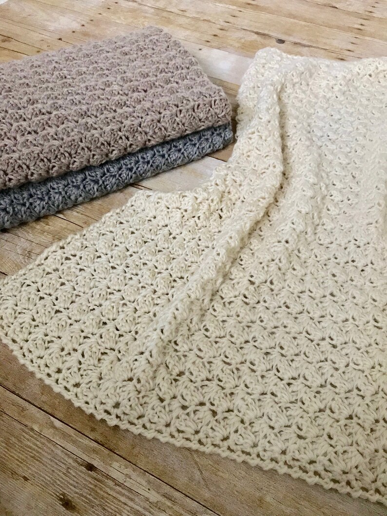 May include: Three crocheted blankets in different colors: beige, gray, and white. The blankets are made with a delicate stitch pattern and have a soft, textured feel.