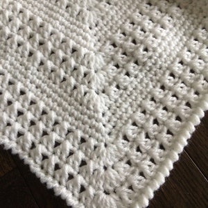 May include: White crochet blanket with a delicate stitch pattern. The blanket has a scalloped edge and is made with a soft, lightweight yarn.